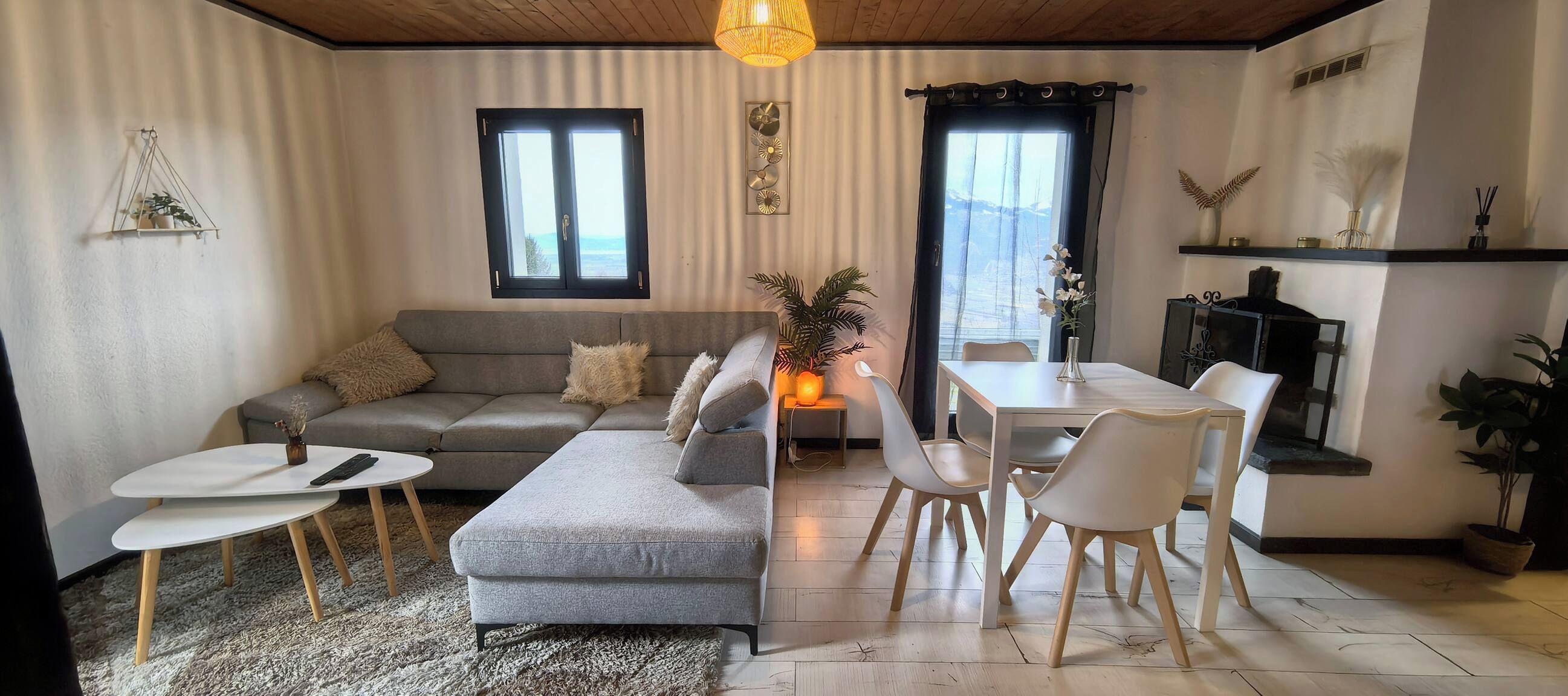 A modern living room with a grey sofa, a dining table with chairs, a small coffee table, and a fireplace.