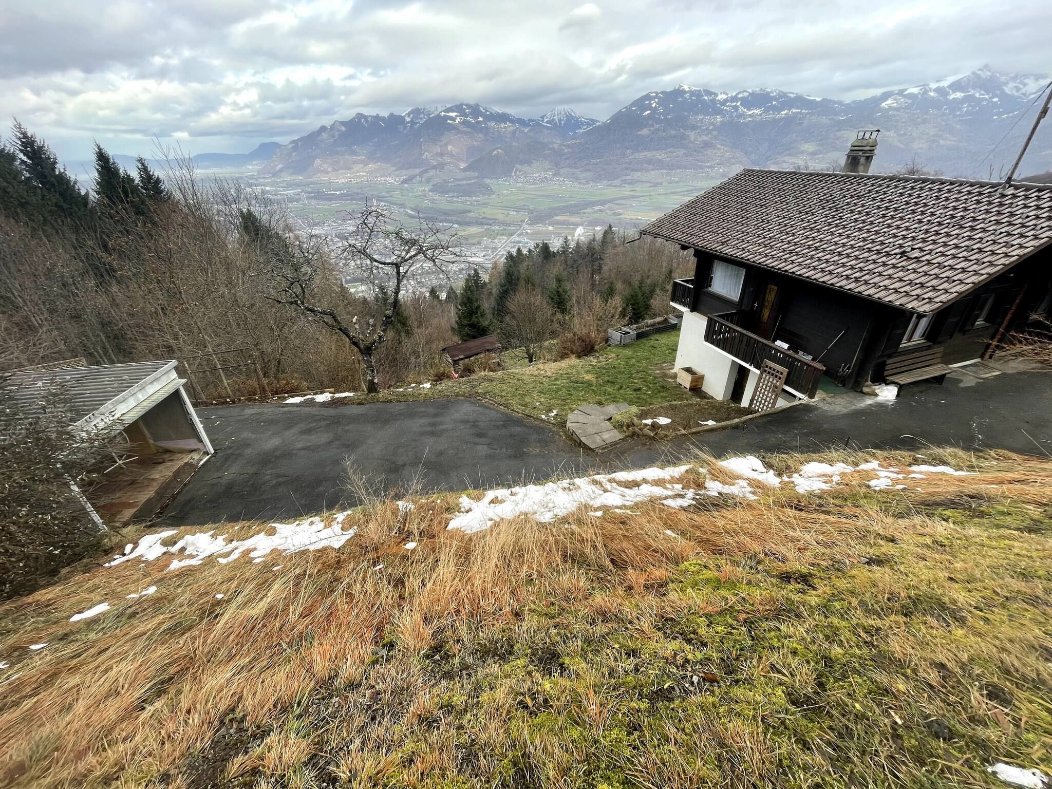 Uma casa com telhado inclinado, garagem e vista para montanhas ao fundo.