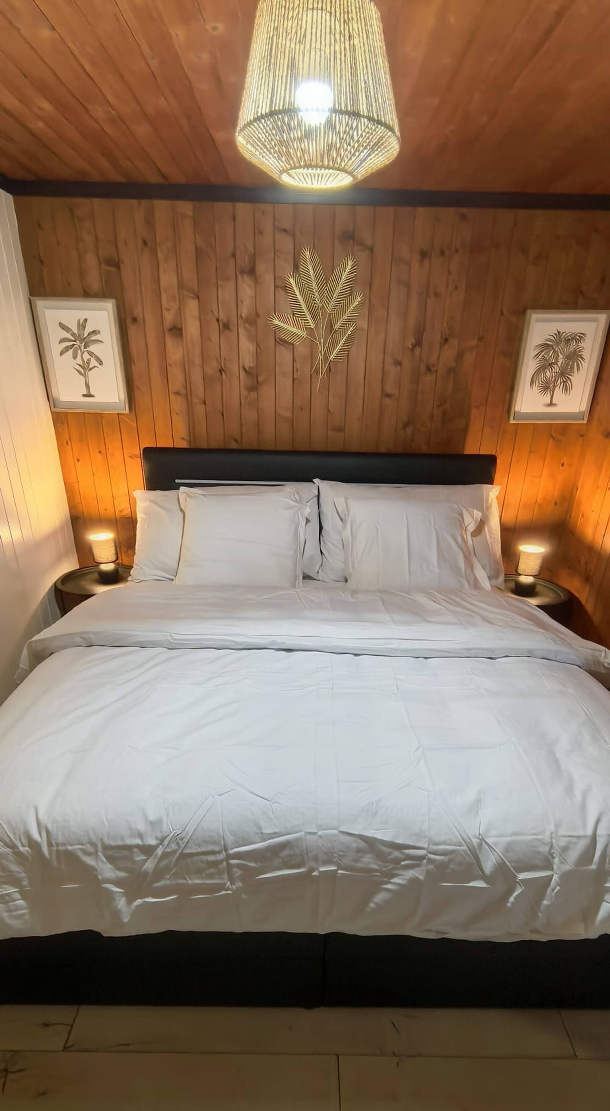 Een bed met witte beddengoed, een houten hoofdeinde en twee wandlampen.