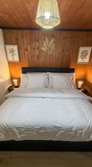 A bed with white bedding, a wooden headboard, and two wall-mounted lamps.