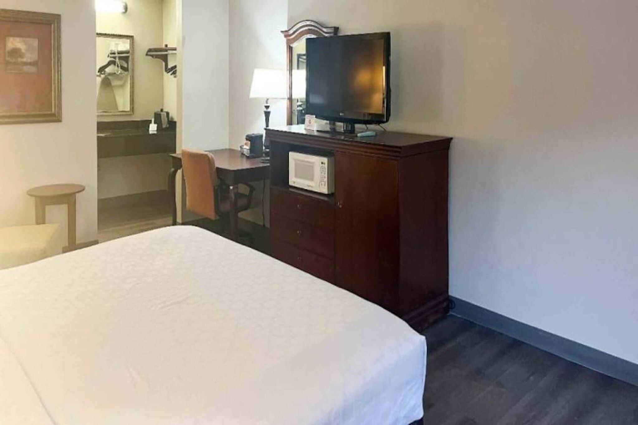 Una habitación de hotel con una cama, un escritorio con una silla, un televisor y un espejo.