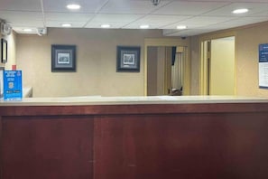 A reception desk with a framed picture on the wall, a blue sign with text, and a door leading to another room.