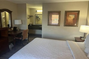 A hotel room with a bed, a desk, a chair, a mirror, and two framed pictures on the wall.