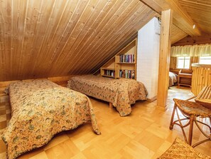 Ein gemütliches Schlafzimmer im Dachgeschoss mit zwei Betten, einem Bücherregal und einem Korbsessel.