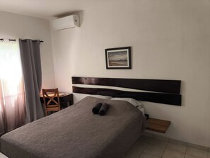 Une chambre à coucher comprenant un lit, une chaise, une table, un tableau au mur et un appareil de climatisation.