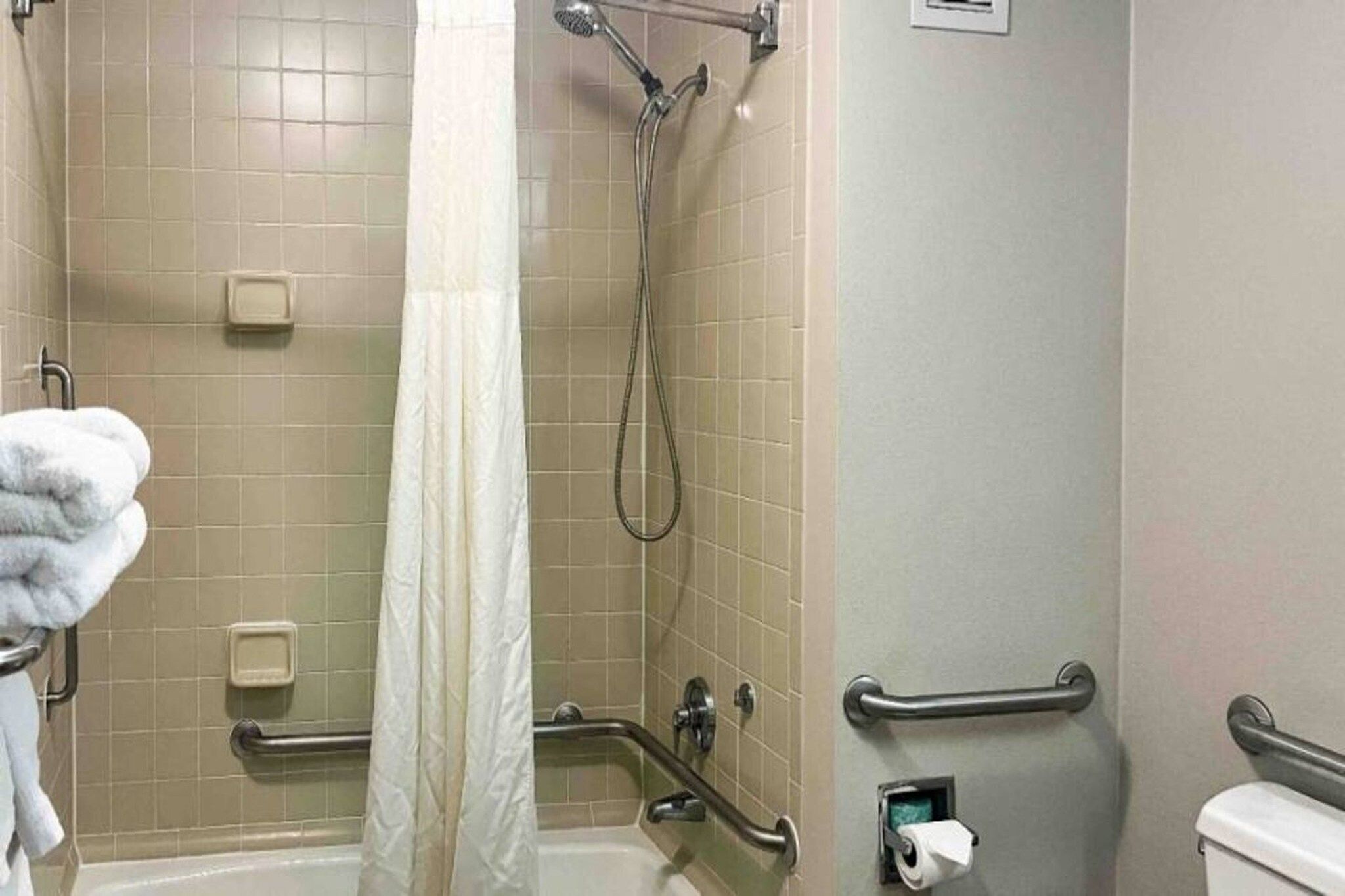 Un baño con bañera, ducha, barras de apoyo, toallero y retrete.