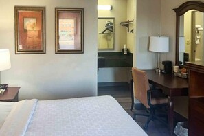 A hotel room with a bed, a desk, a chair, a mirror, and a bathroom visible through an open door.