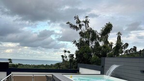 Una terraza en la azotea con jacuzzi, taburetes de bar y vista al océano.