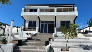 Una casa moderna de dos pisos con techo plano, ventanas grandes y una escalera que conduce a la entrada.