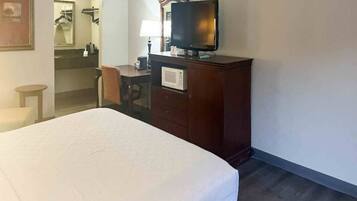 Een hotelkamer met een bed, een bureau met stoel, een televisie en een spiegel.