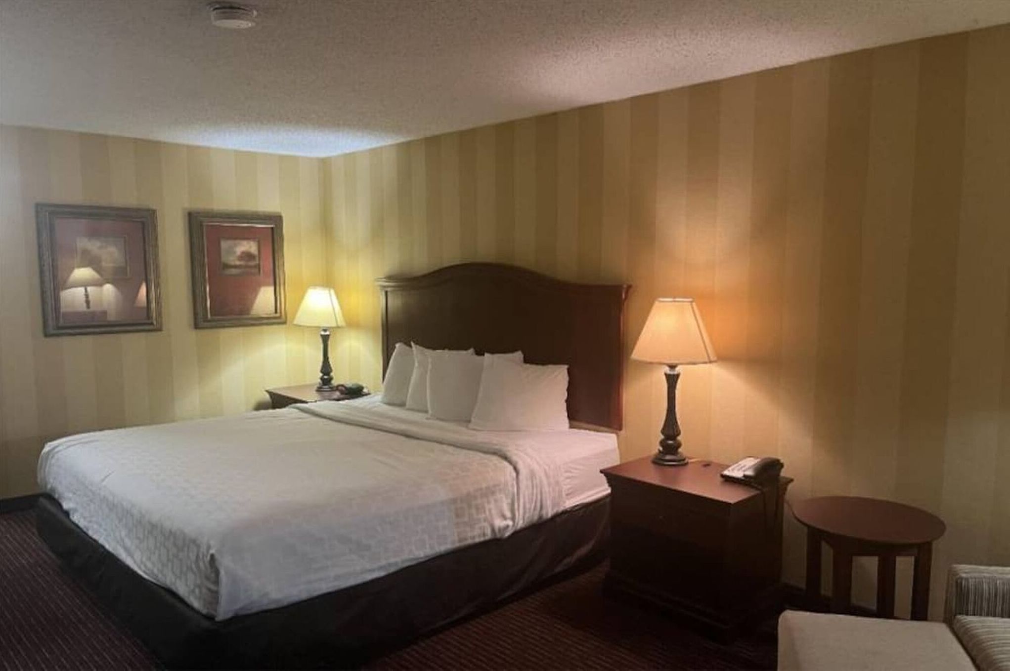 Een hotelkamer met een groot bed, twee nachtkastjes met lampen, een stoel en twee ingelijste foto's aan de muur.