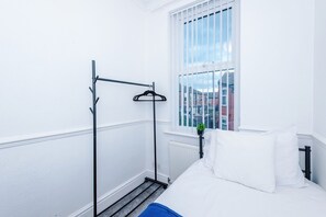 Een kamer met een bed, een radiator, een raam met tralies en een kledingrek.