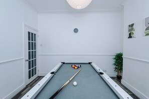 Ein Billardtisch mit Kugeln und Spielstock, eine Uhr an der Wand und eine Tür mit Fensterfeldern.