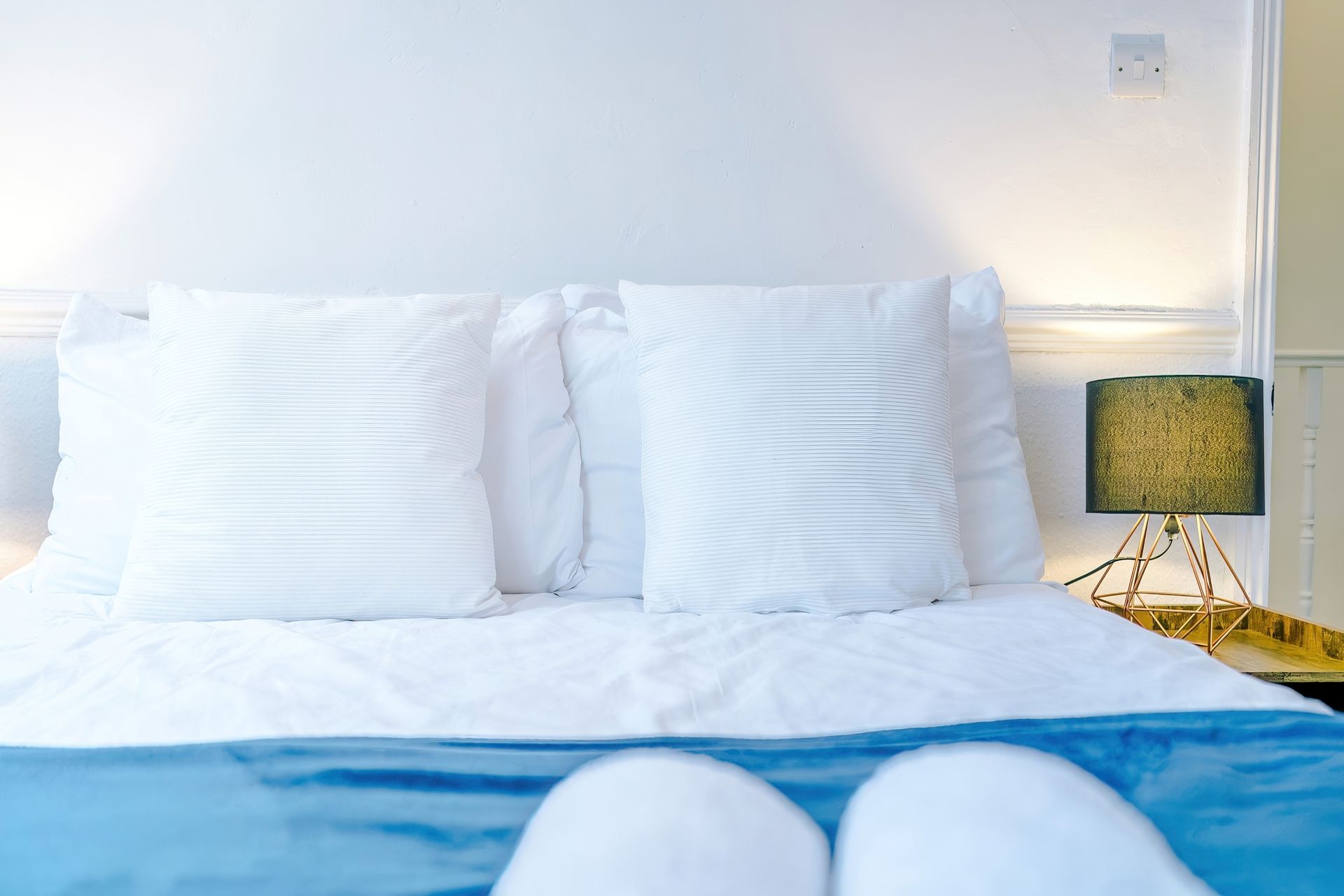 A bed with white bedding and two pillows, a bedside lamp, and a wall socket.