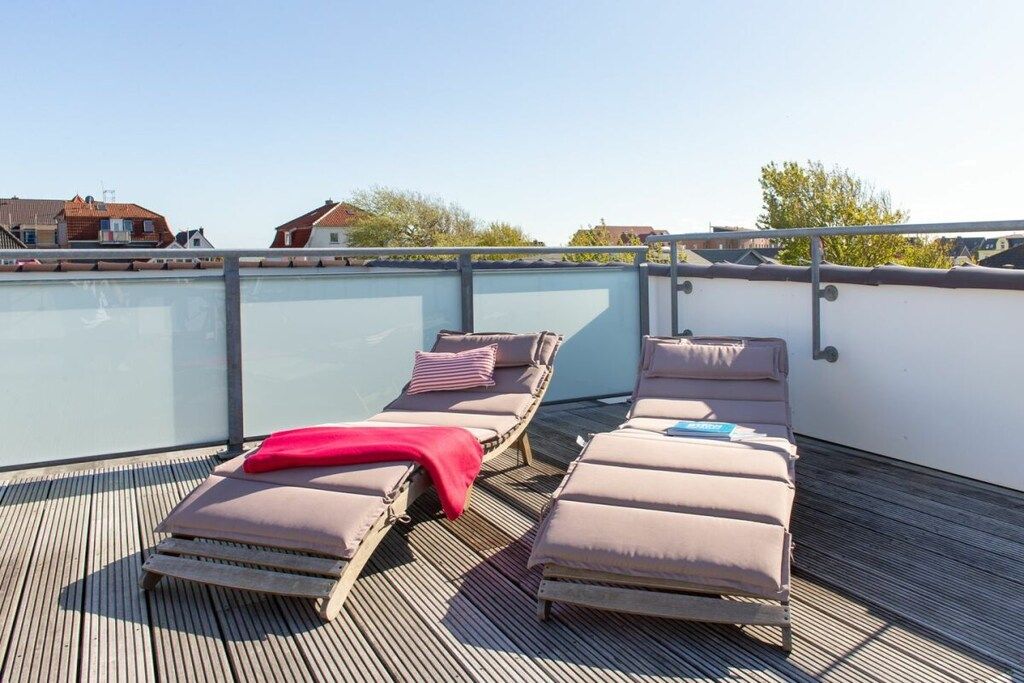 Une terrasse sur le toit équipée de deux chaises longues, dont l’une est agrémentée d’une couverture rouge et de coussins, et l’autre d’une serviette bleue.