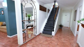 A staircase leading to a second floor, a mirror with a decorative frame, a potted plant, and a tiled floor.