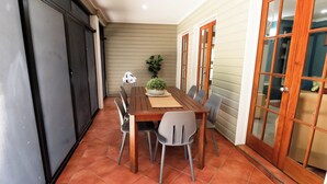 Un coin repas avec une table en bois, quatre chaises, une plante en pot et une porte-fenêtre coulissante.