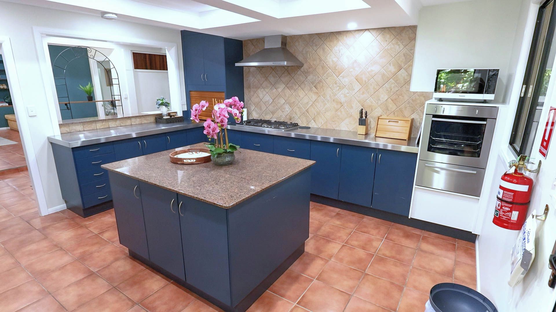 A modern kitchen with a central island, blue cabinets, a gas stove, and a stainless steel oven.