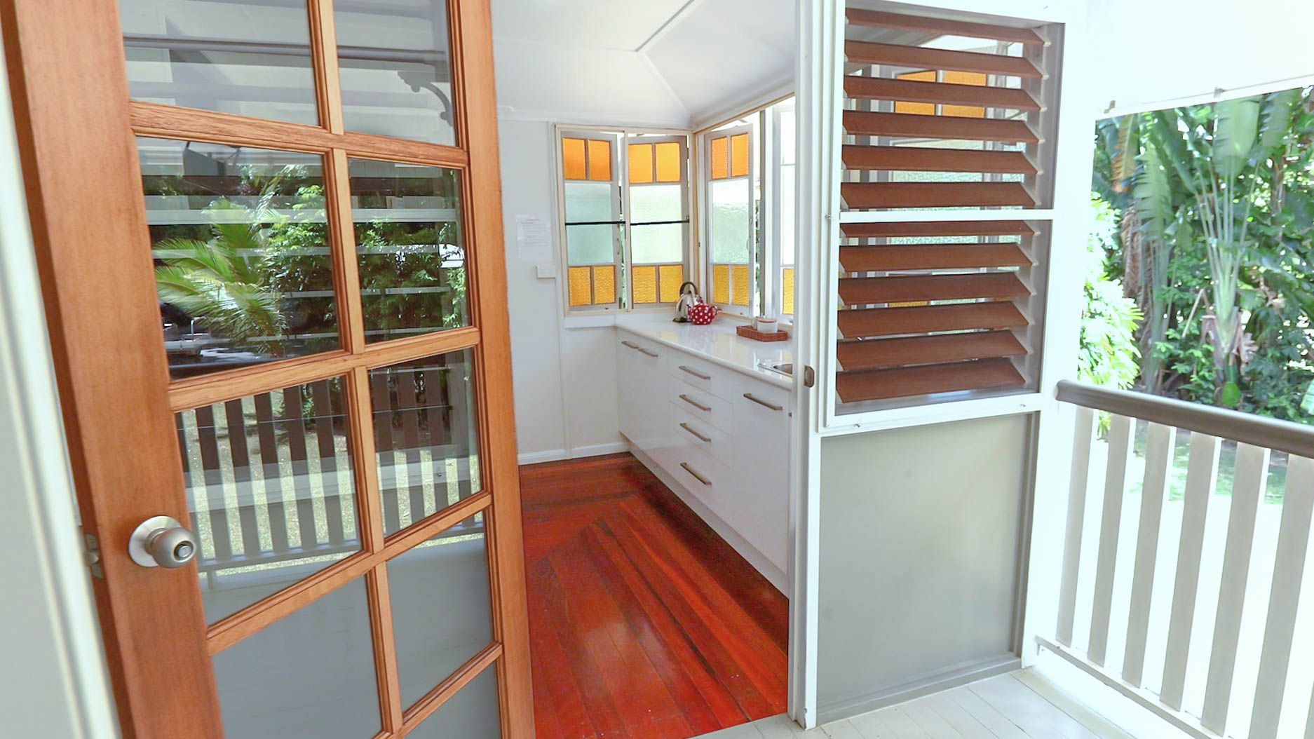A room with a wooden door, a white cabinet, a mirror, and a view of greenery outside.