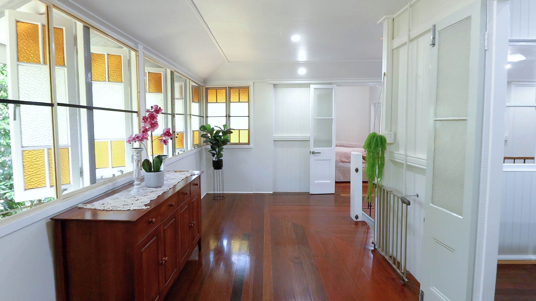 A hallway with wooden flooring, a wooden bench with a white tablecloth, and potted plants.