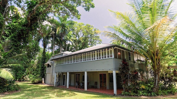 A two-story house with a covered porch, surrounded by lush greenery and trees.
