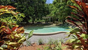 Une piscine entourée d’un jardin où poussent différentes espèces de plantes, ainsi qu’un espace salon abrité.