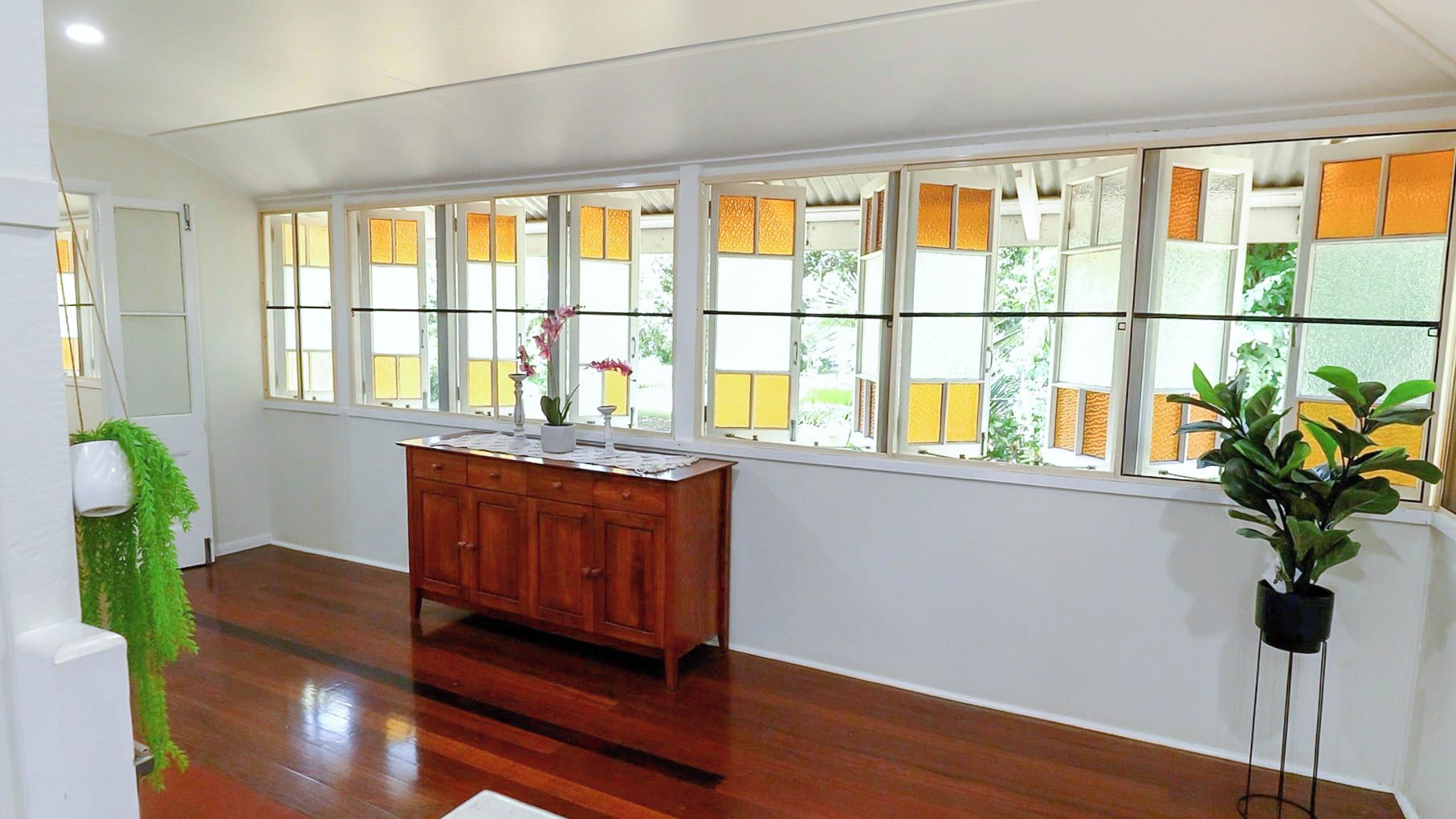 A room with a wooden floor, a wooden cabinet, and a large window with multiple panes.