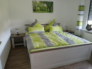 Een slaapkamer met een bed, twee nachtkastjes, een nachtlampje, een schilderij aan de muur en een raam met zonwering.