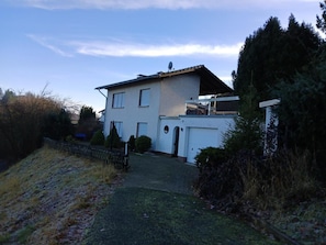 Een tweelaags huis met een garage, een overdekte veranda en een omheinde tuin.