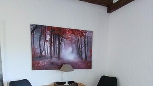 Huoneen nurkassa on puinen pöytä, kaksi mustaa tuolia, metsäaiheinen maalaus ja katossa näkyvillä olevat puupalkit.