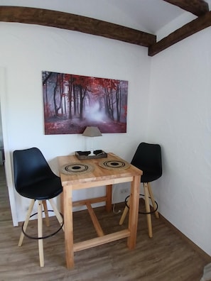 Een hoekappartement met een houten tafel, twee zwarte stoelen, een schilderij van een bos en zichtbare houten balken aan het plafond.