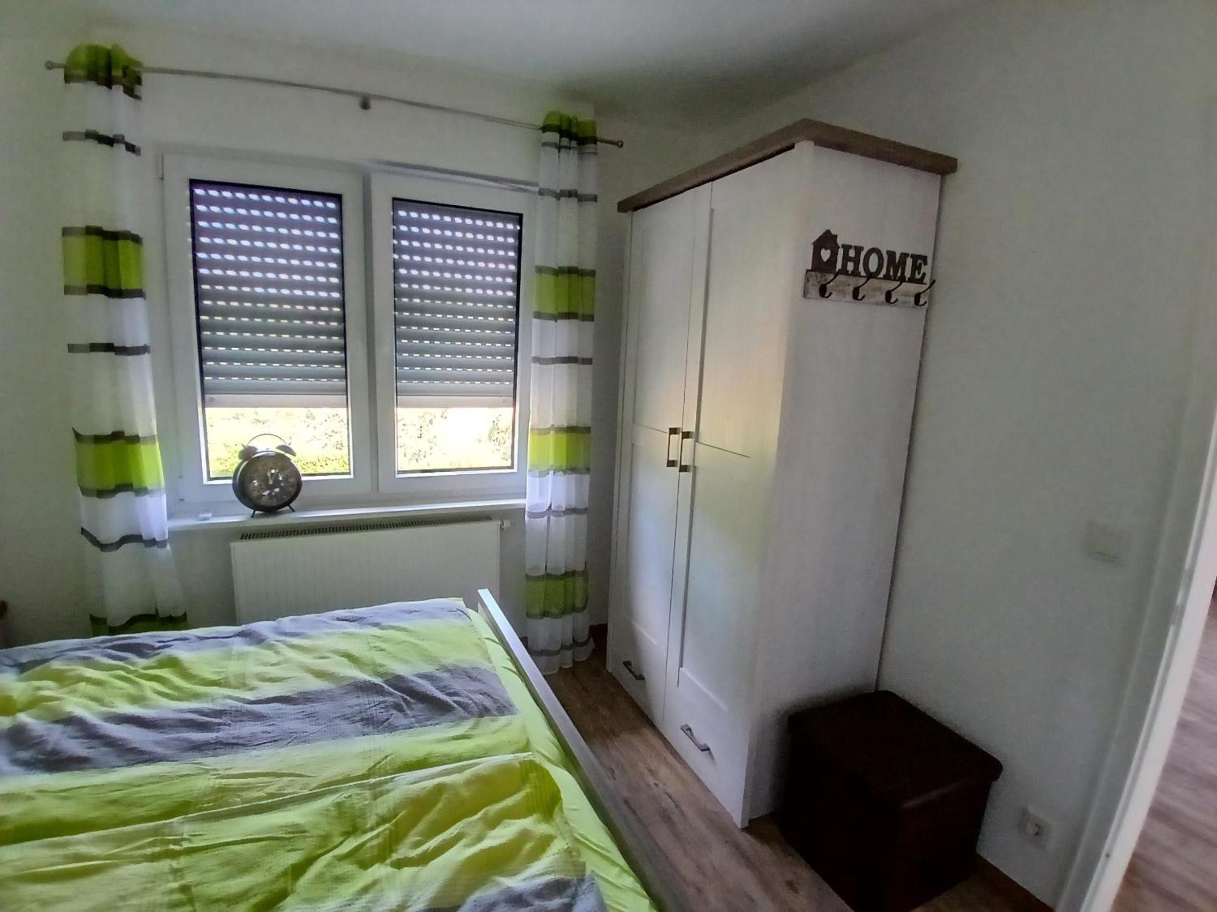 Ein Schlafzimmer mit Bett, Kleiderschrank, einem Fenster mit Jalousien und einem Heizkörper.