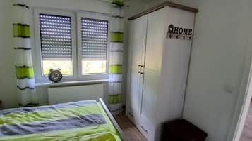 Ein Schlafzimmer mit Bett, Kleiderschrank, einem Fenster mit Jalousien und einem Heizkörper.