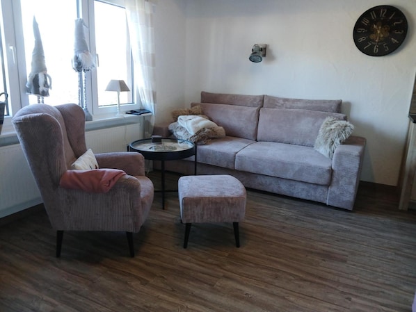 Een woonkamer met een bank, fauteuil, poef en een klein rond tafeltje.