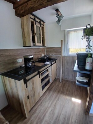A compact kitchen with wooden cabinets, a black countertop, and a window with blinds. - Auszeit zu Zweit Apartment with Garden View in the Sauerland (Medebach)
