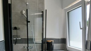 Moderni kylpyhuone, jossa on lasiseinällä varustettu suihku, wc ja pesuallas.