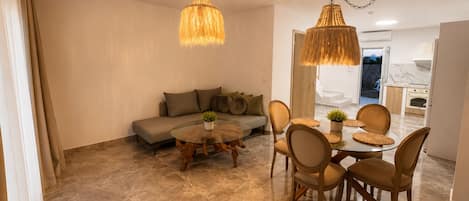 A modern living room with a sofa, a round glass coffee table, and a dining area with a table and chairs.