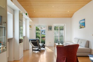 Et moderne interiør med træloft, spiseplads med et glasbord, en rød stol og en sofa.