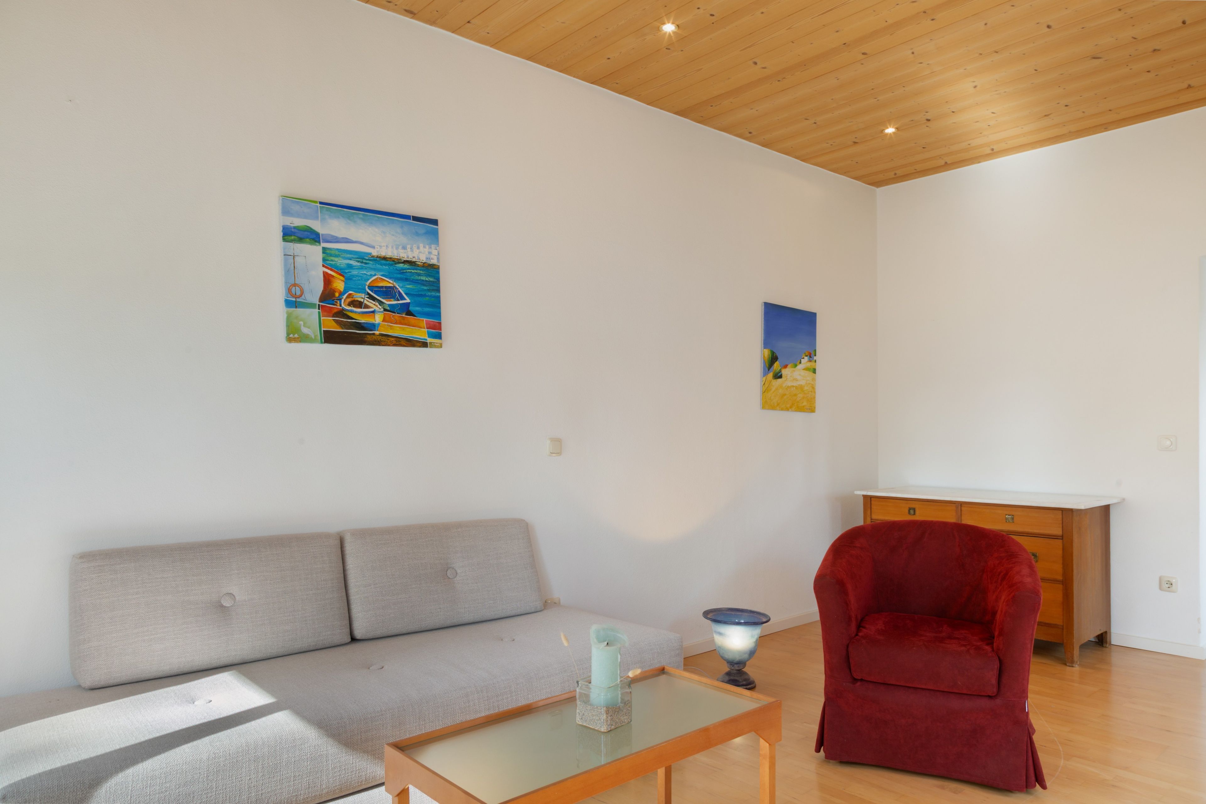 A living room with a sofa, a red chair, a glass coffee table, and two paintings on the wall.
