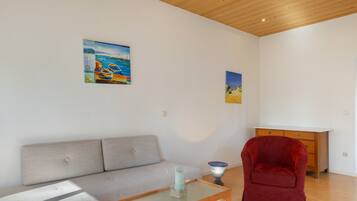 A living room with a sofa, a red chair, a glass coffee table, and two paintings on the wall.
