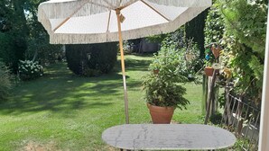 Um jardim com uma mesa redonda e um guarda-sol suspenso.