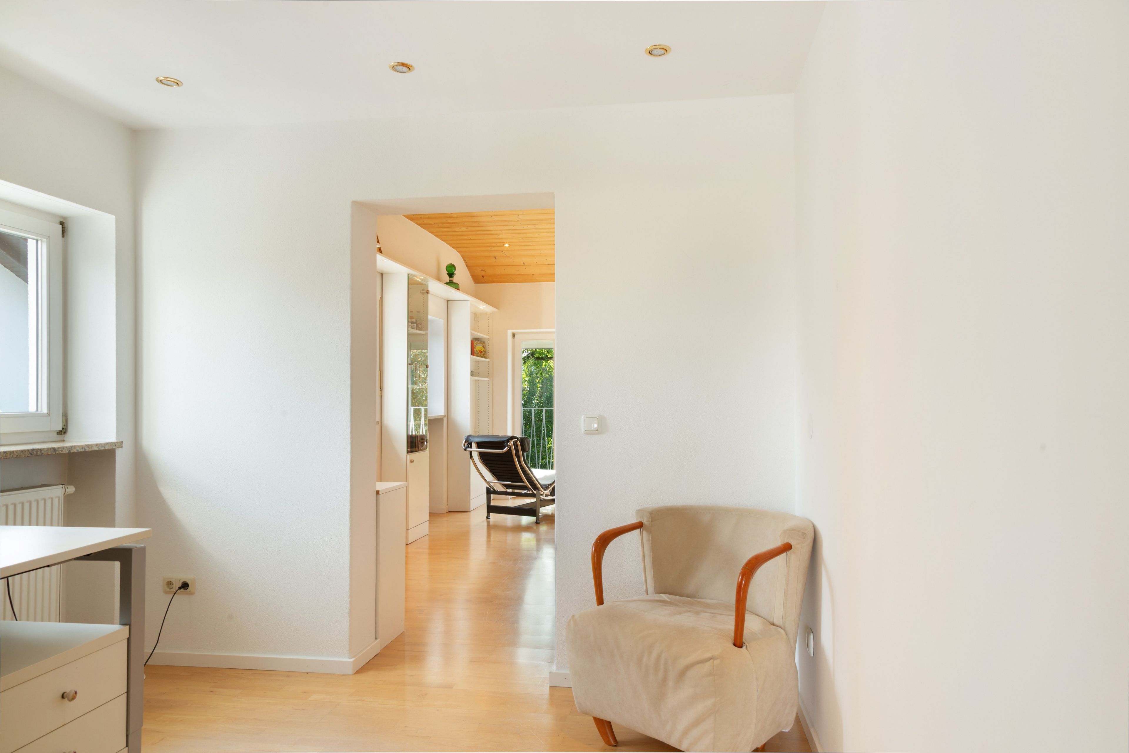 A modern interior with a wooden floor, a chair, and a view through an open door leading to a balcony.