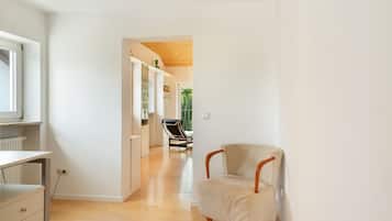 A modern interior with a wooden floor, a chair, and a view through an open door leading to a balcony.