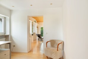 Et moderne interiør med trægulv, en stol og udsigt gennem en åben dør til en balkon.