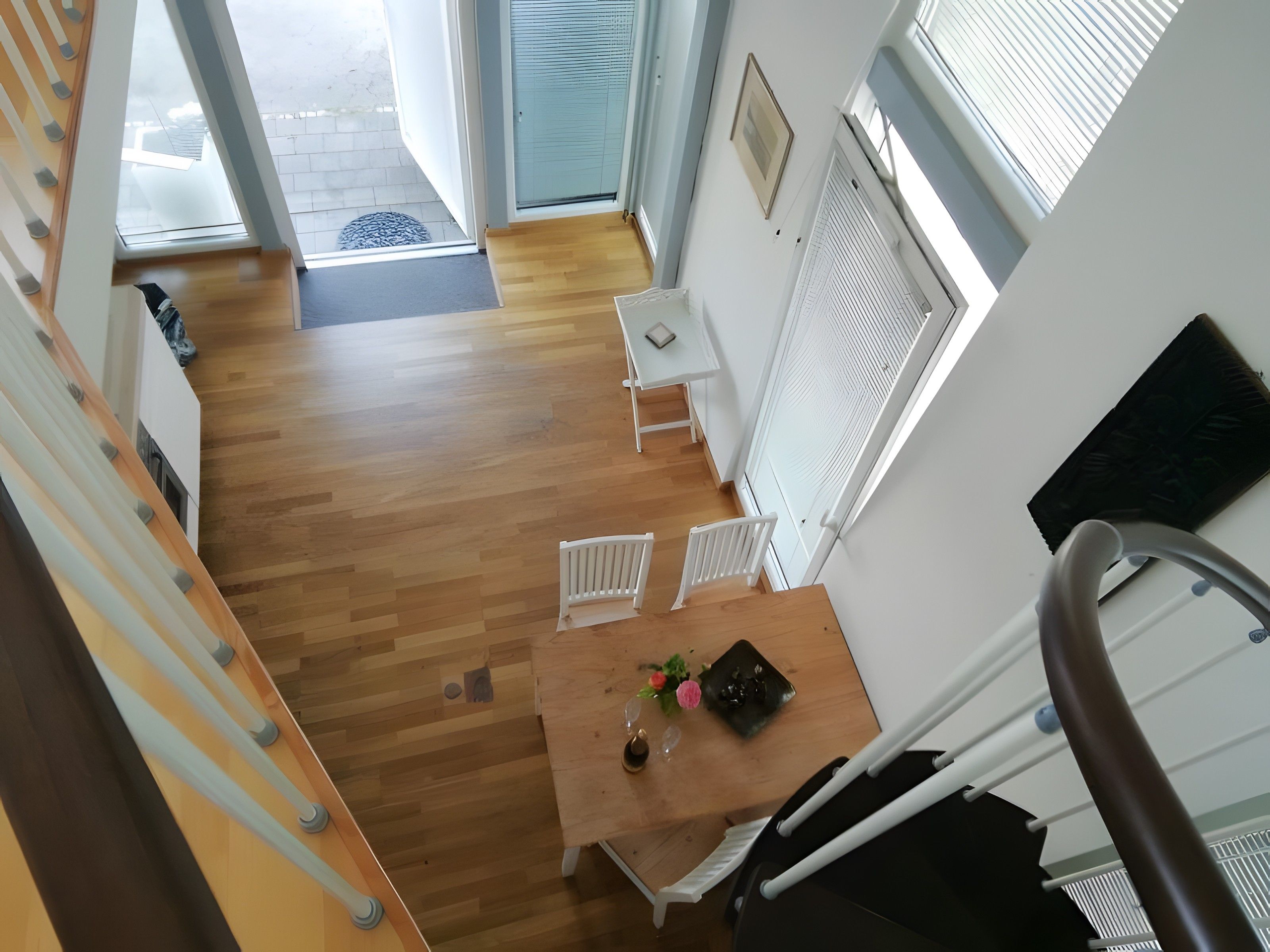 Ein Zimmer mit hohen Decken, Holzboden, einem weißen Tisch mit Stühlen, einem kleinen Fenster und einer Tür, die nach draußen führt.
