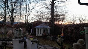 Um jardim com um gazebo, uma mesa e cadeiras, e diversas plantas.