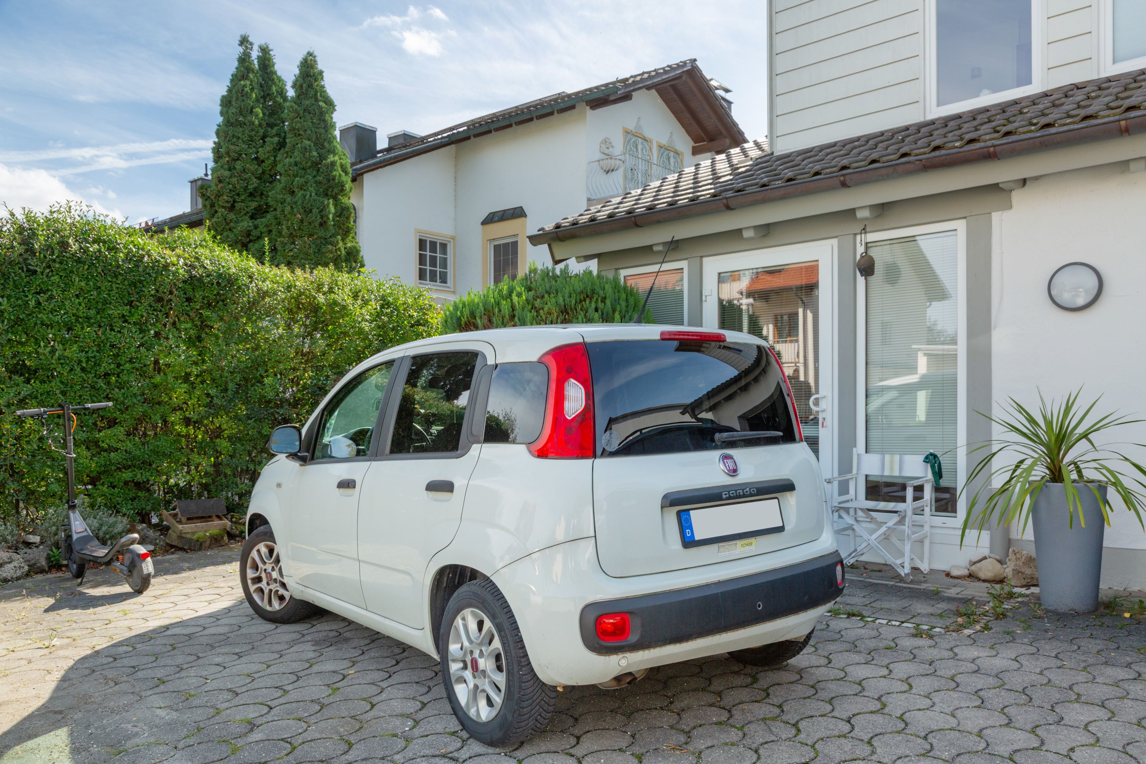 A white car parked in front of a house with a tiled roof and a white exterior.