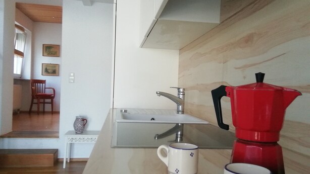 Cozinha com pia, cafeteira vermelha e duas canecas brancas com estampas azuis.