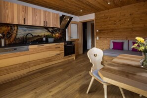 A modern kitchen with wooden cabinetry, a built-in oven, and a dining area with a wooden table and a single chair. - Morgenstern Mountain Farm Schoberlehen (Bischofswiesen)