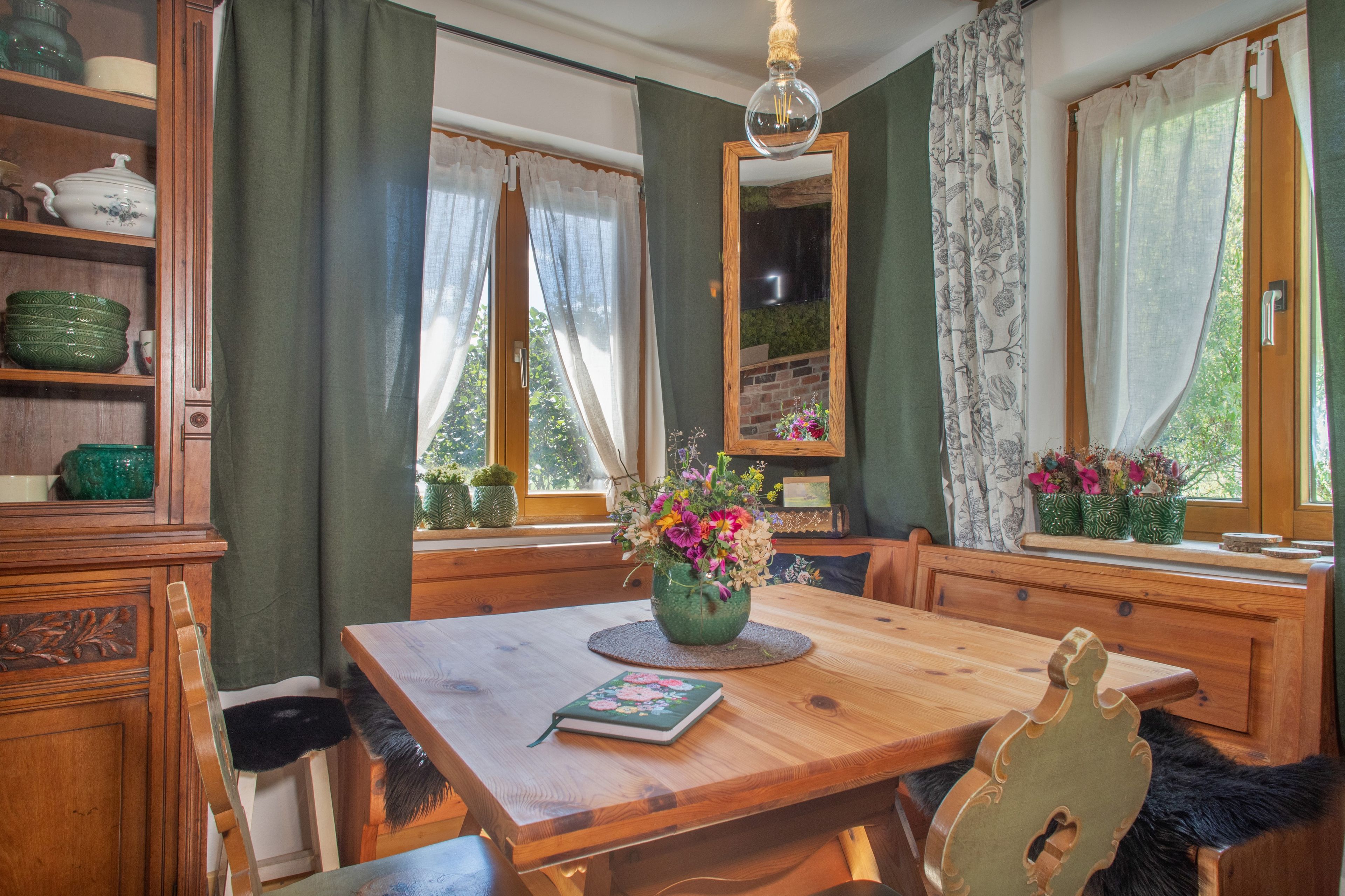 A dining room with a wooden table, chairs, a vase of flowers, and a mirror on the wall.